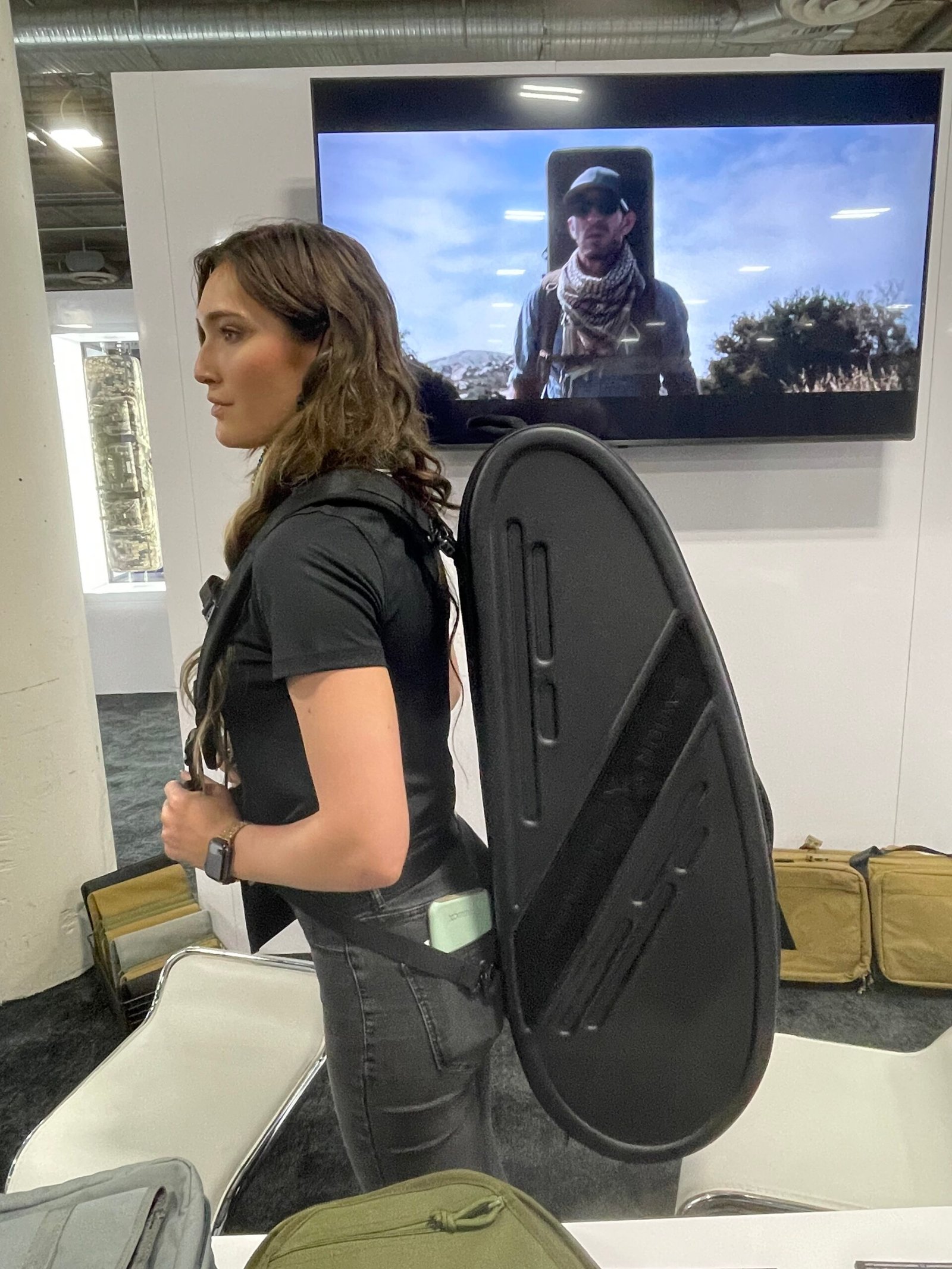 Mulher demonstra mochila rígida para transporte de arma longa.