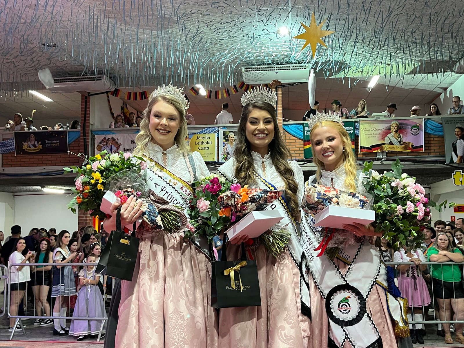 Rainhas da Schützenfest posam com coroas, faixas, flores e rifle cerimonial.
