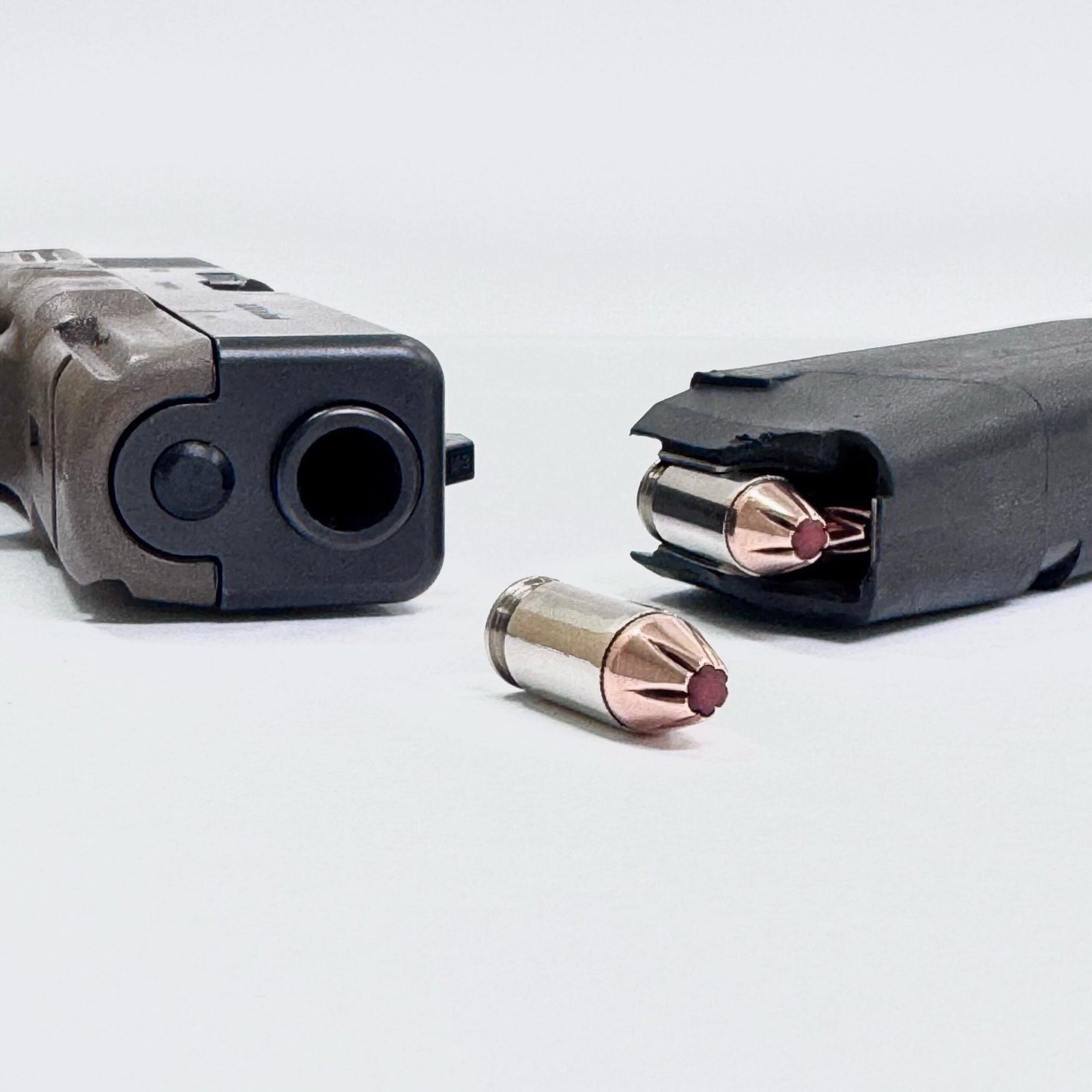 Cano de pistola, carregador e cartuchos calibre .380 ACP sobre fundo branco.