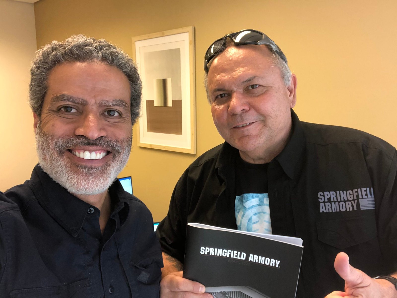 Demetrius Oliveira posa com representante da Springfield Armory segurando catálogo.