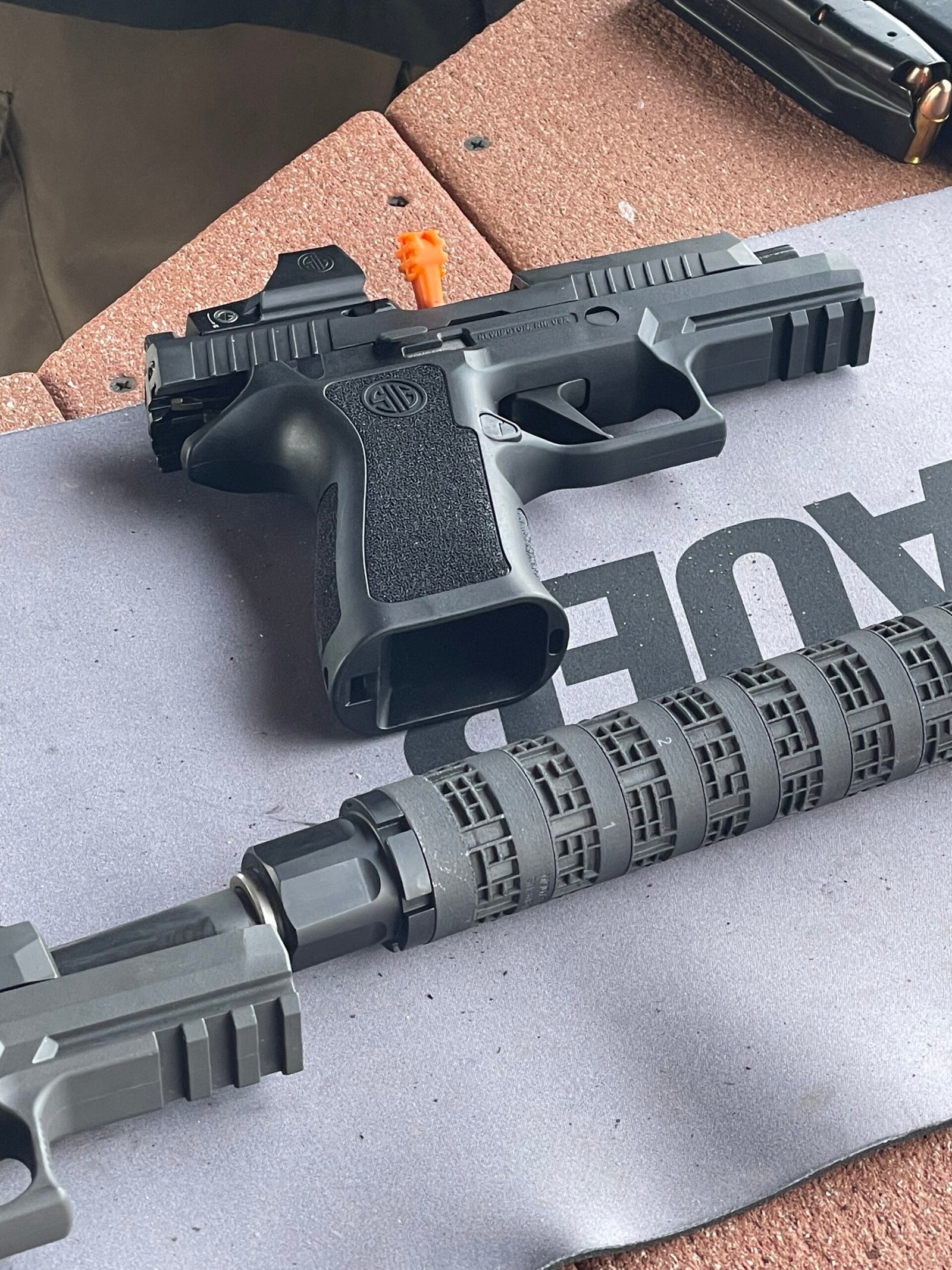 Pistola e arma longa apoiadas sobre bancada em campo de tiro.