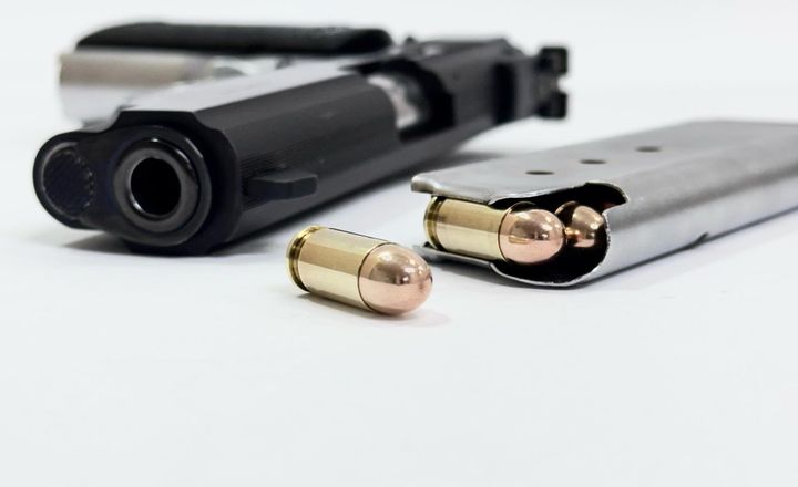 Pistola e cartuchos calibre .380 ACP sobre fundo branco.