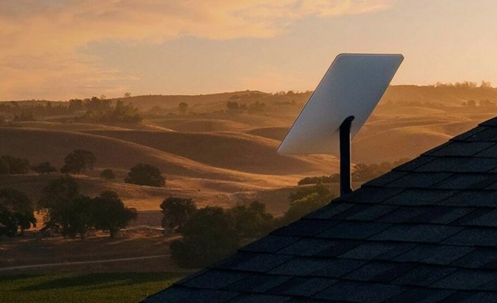 Antena Starlink instalada em telhado diante de paisagem rural ao pôr do sol.