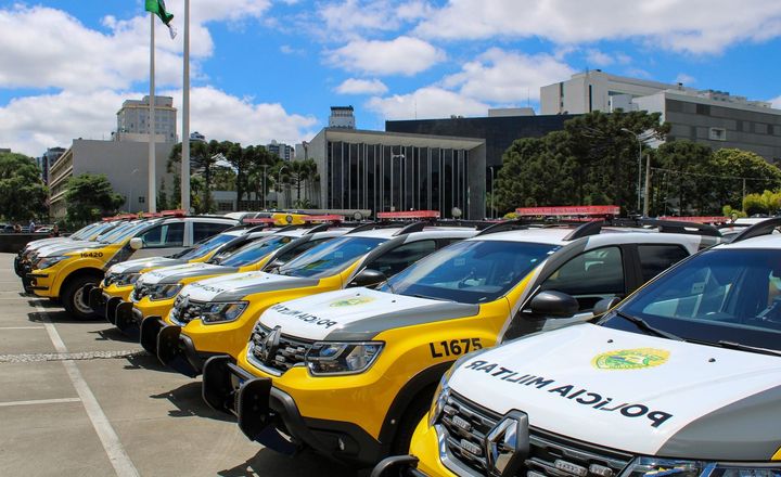 Fileira de viaturas policiais estacionadas diante de prédio público do Paraná.