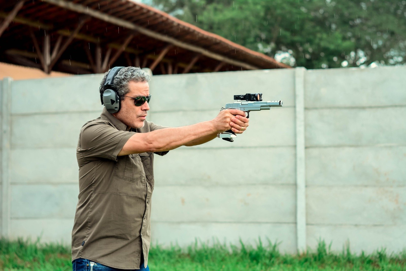 Demetrius Oliveira aponta pistola em campo de tiro ao ar livre.