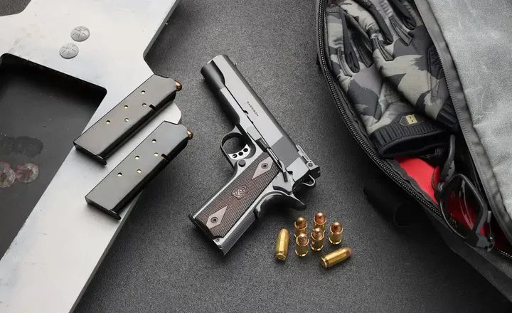 Pistola Springfield Armory 1911, carregadores e munição sobre bancada.