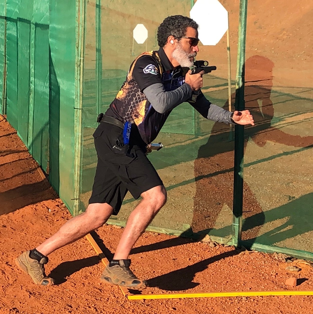 Atirador percorre pista de tiro prático com pistola em movimento.