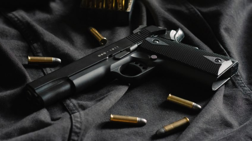 Pistola preta e cartuchos sobre tecido escuro.
