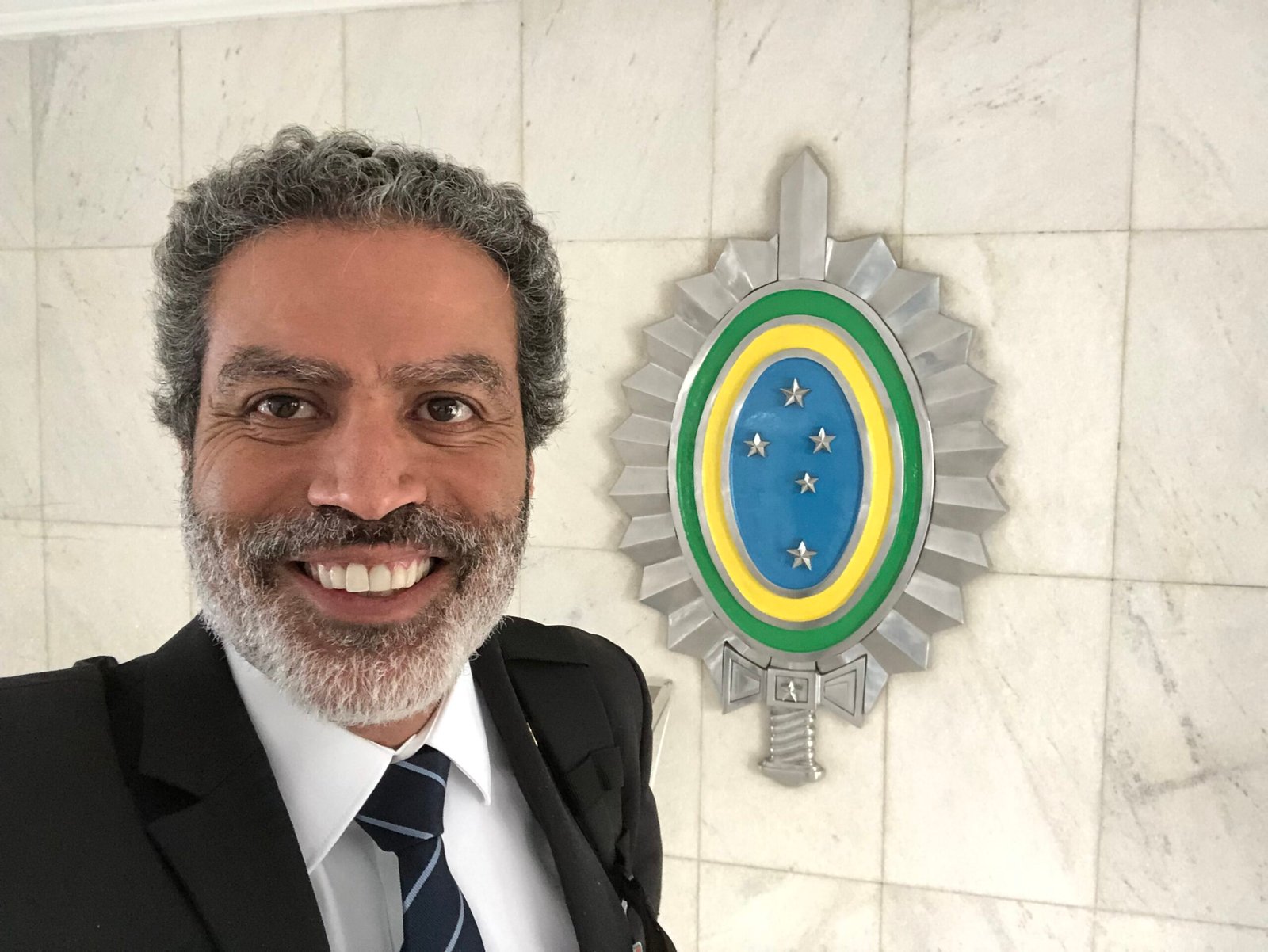 Demetrius Oliveira posa sorrindo diante de brasão do Exército.