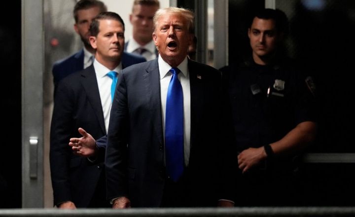 Donald Trump fala a jornalistas ao sair de um edifício acompanhado por assessores.