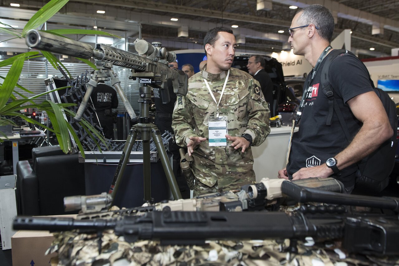 Militar conversa com expositor diante de armamentos na LAAD.