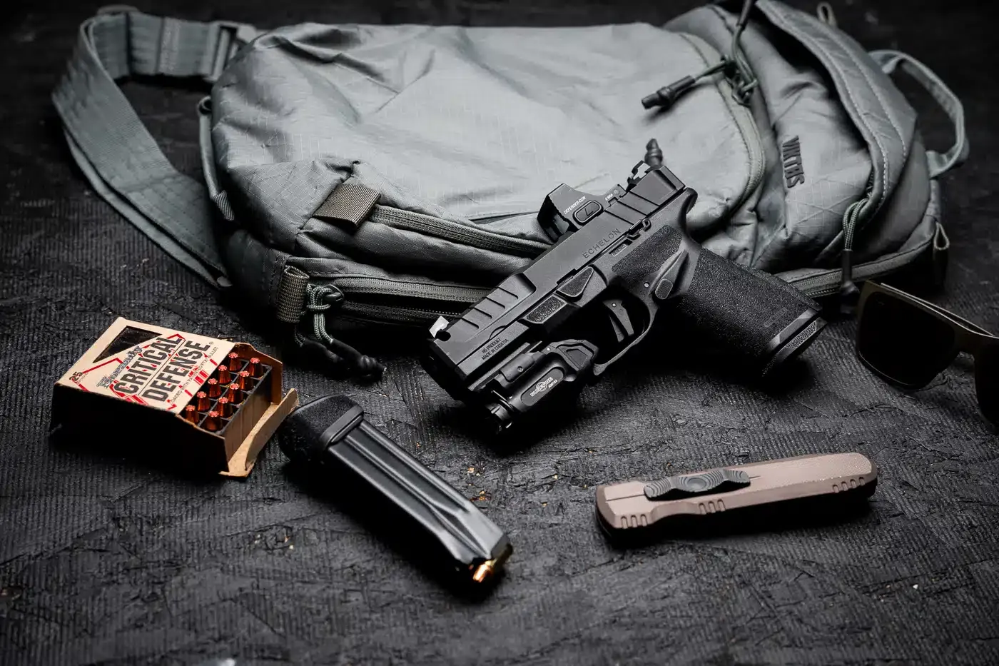 Pistola Echelon 4.0C Comp com carregadores, munição e canivete sobre bolsa aberta.