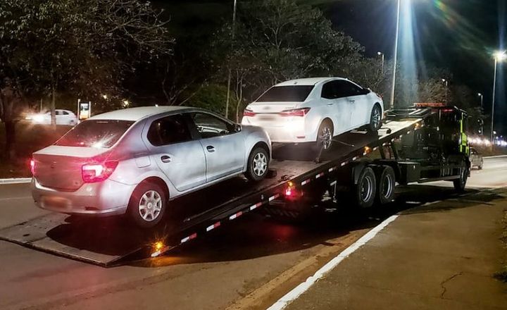 Automóveis são transportados por caminhão-guincho durante a noite.