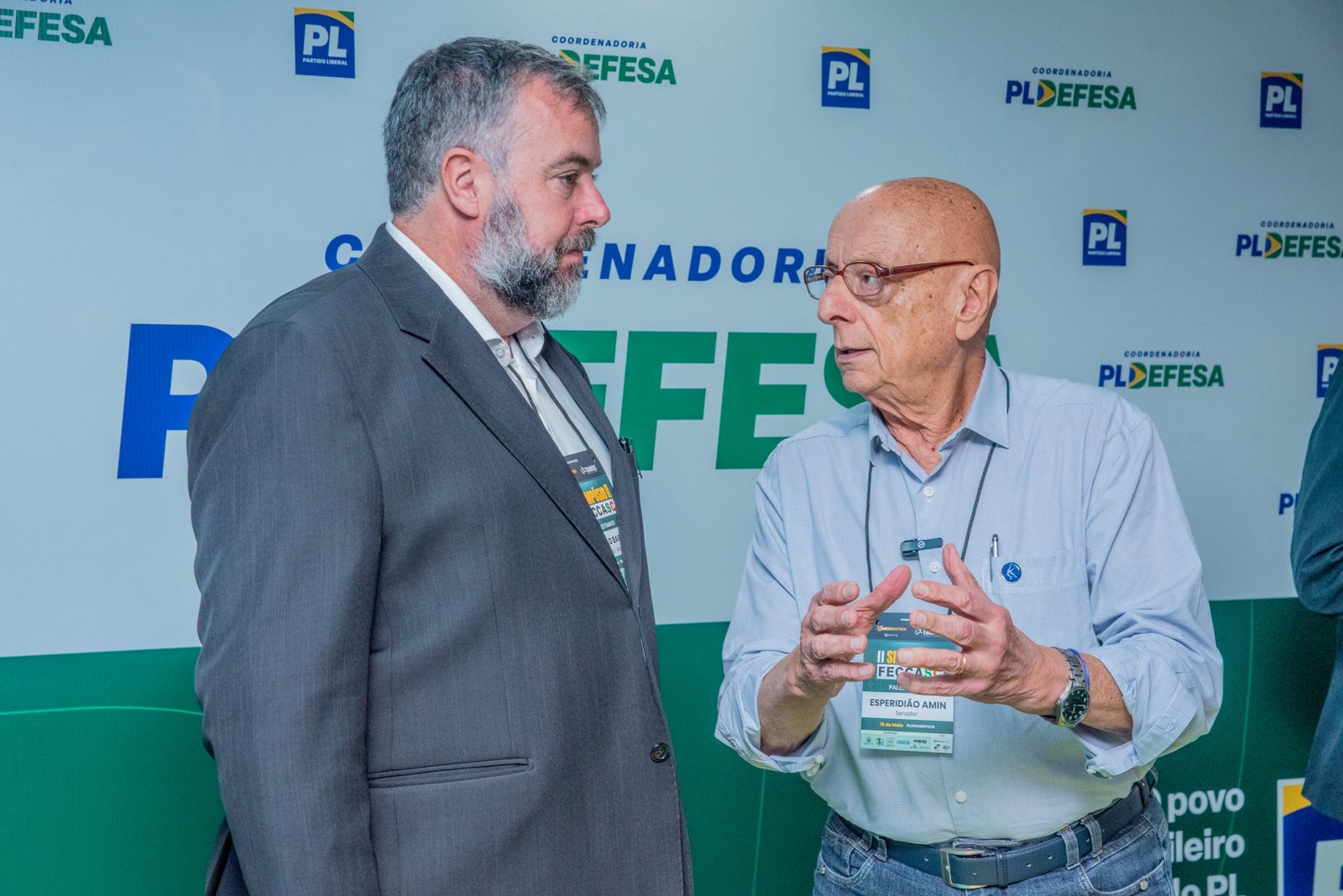 Dois participantes conversam diante do painel PL Defesa.