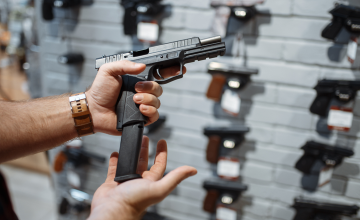 Pessoa segura uma pistola com carregador alongado dentro de uma loja de armas.