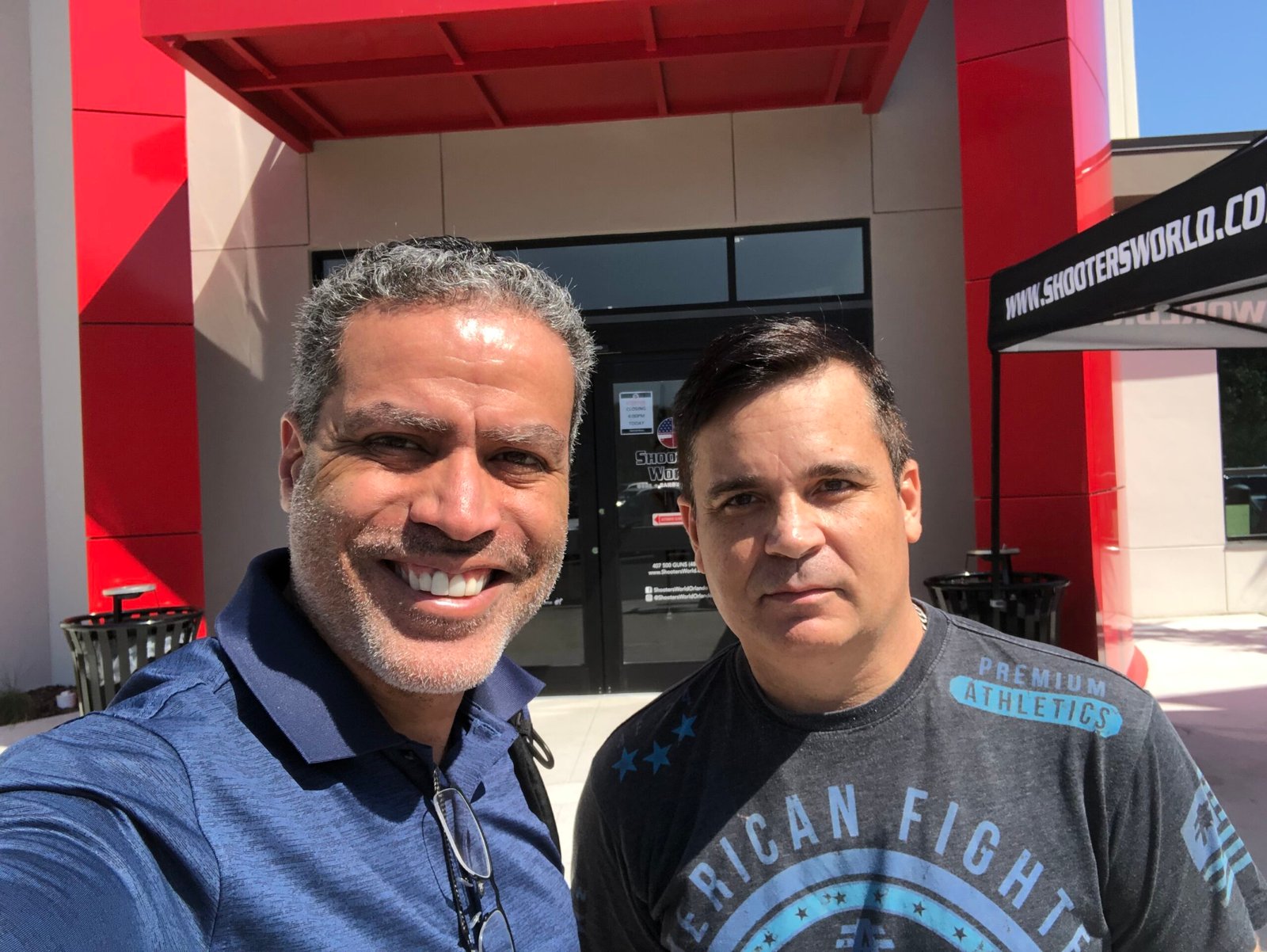 Demetrius Oliveira posa com colega diante de centro de tiro nos Estados Unidos.
