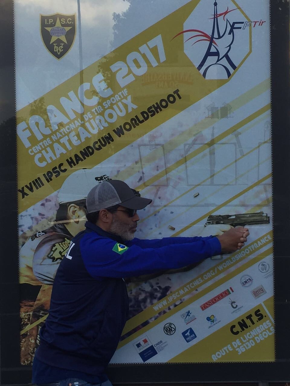 Demetrius Oliveira aponta pistola diante do painel do Mundial de Tiro Prático de 2017.