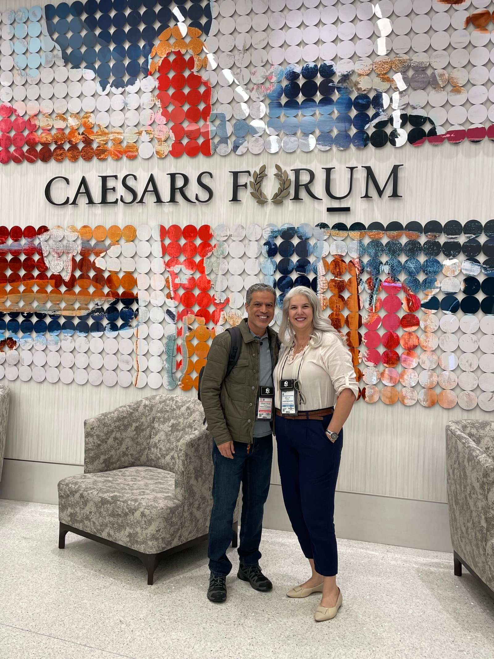 Demetrius Oliveira e uma mulher posam diante do painel do Caesars Forum.