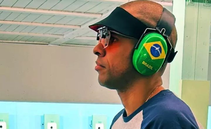 Atirador brasileiro usa óculos e abafador com bandeira do Brasil.