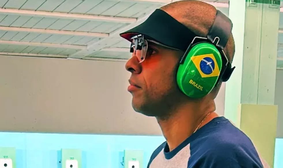 Atirador brasileiro usa óculos e abafador com bandeira do Brasil.