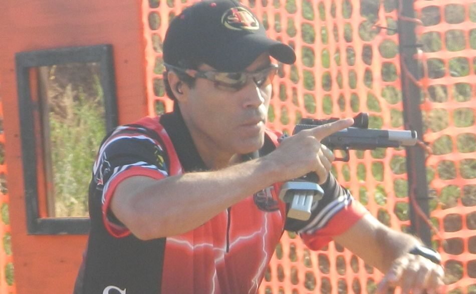 Atirador percorre pista de tiro prático vestindo uniforme vermelho e preto.