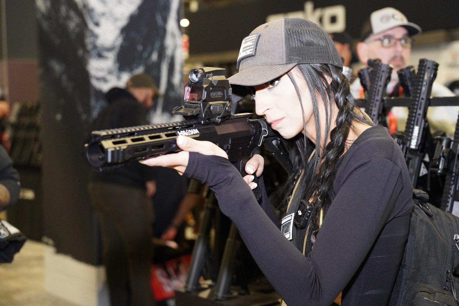 Mulher aponta arma longa equipada com mira durante demonstração.