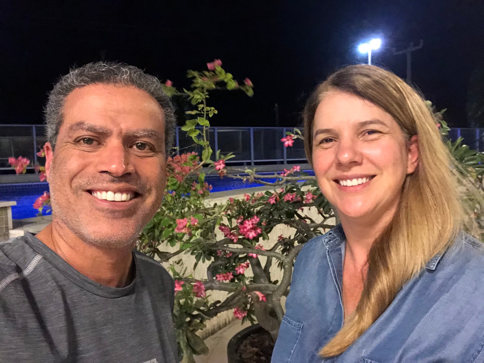 Demetrius Oliveira tira selfie com uma mulher em área externa à noite.