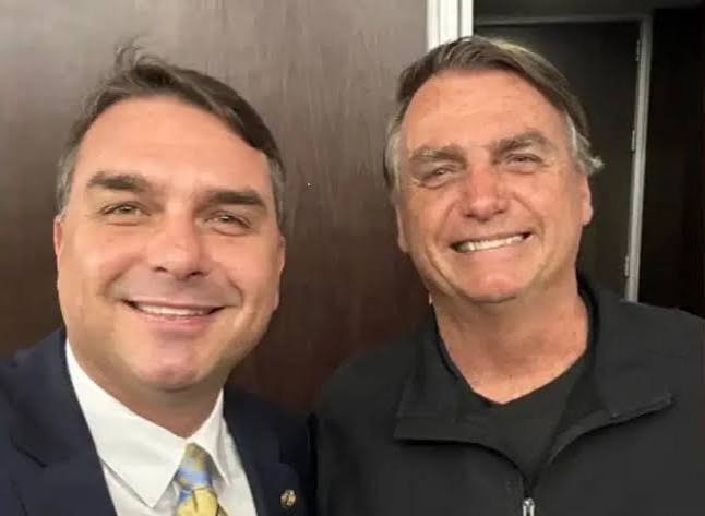 Dois homens sorriem juntos em uma fotografia de retrato em ambiente interno.