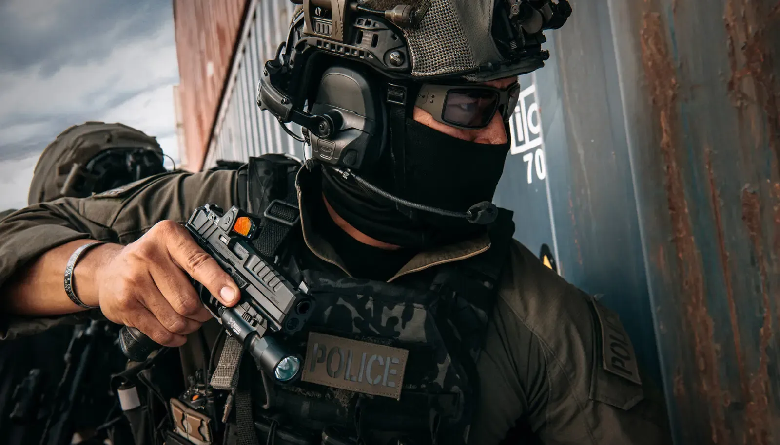 Policial de equipe tática aponta uma pistola durante operação.