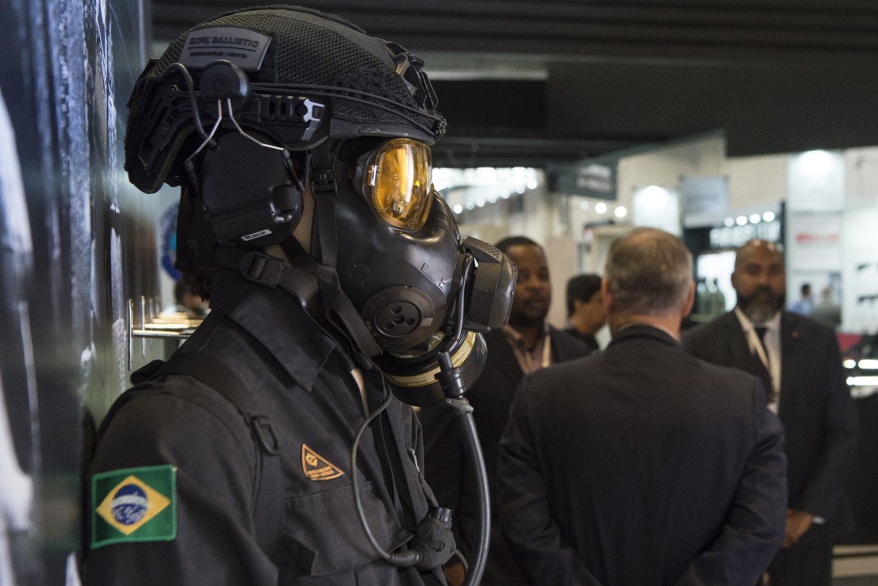 Operador usa capacete, máscara e uniforme tático com bandeira do Brasil.