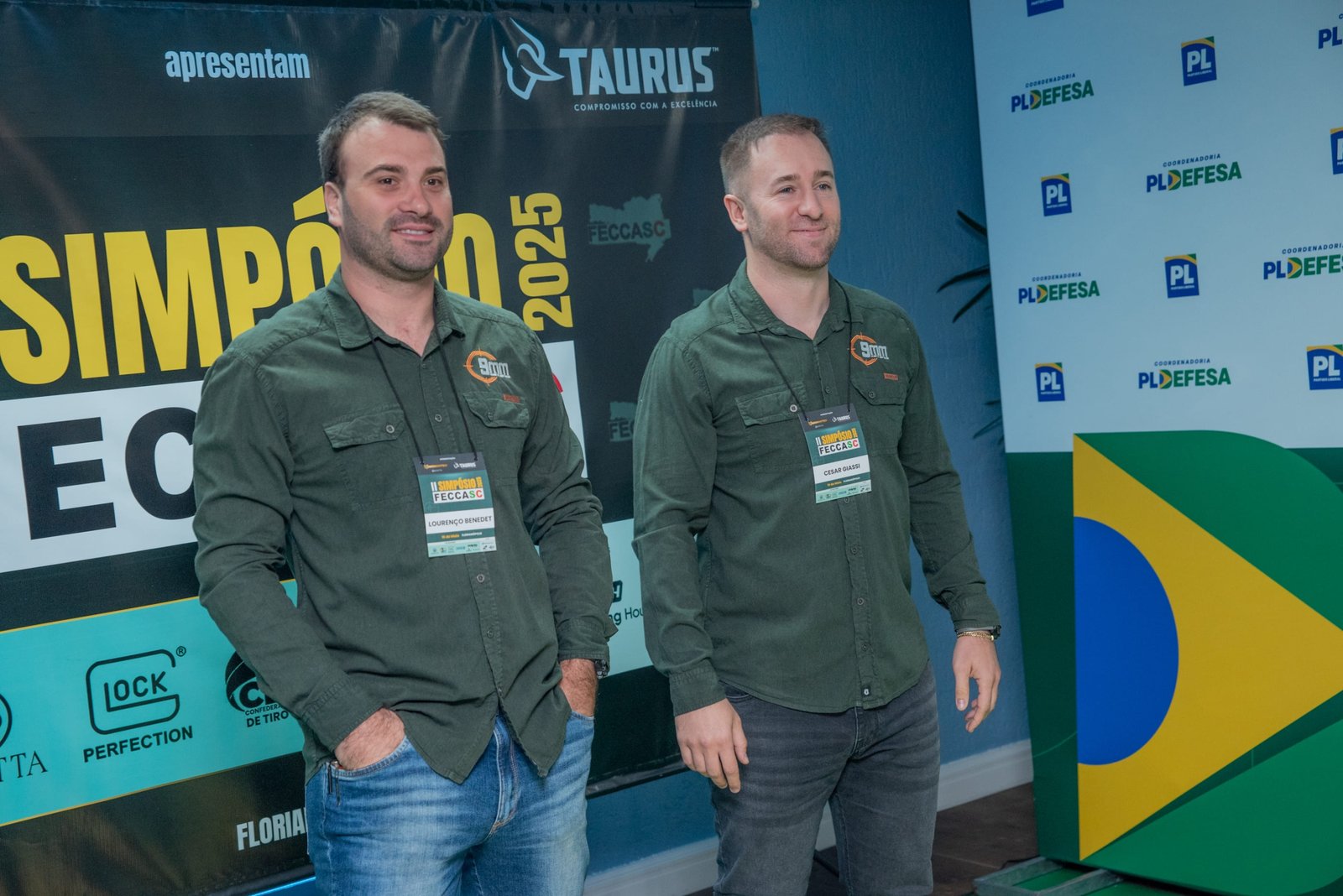 Dois participantes posam diante do painel do Simpósio FECCASC.