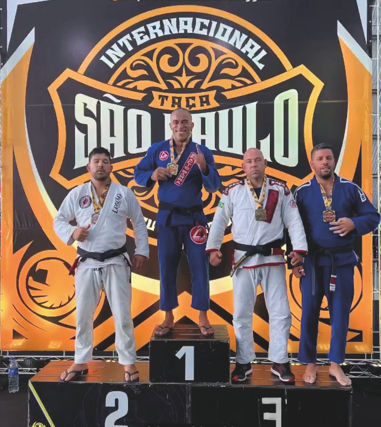 Léo Rocha e outros atletas ocupam o pódio após competição de jiu-jítsu.