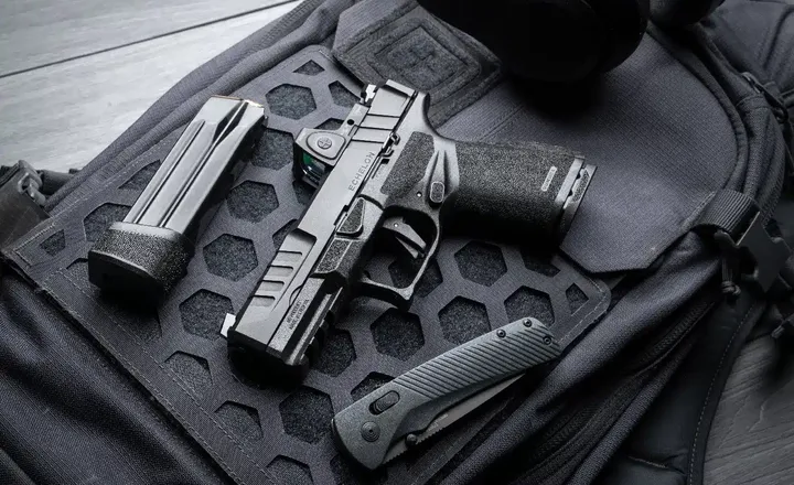 Pistola, carregador e canivete apoiados sobre uma bolsa tática preta.