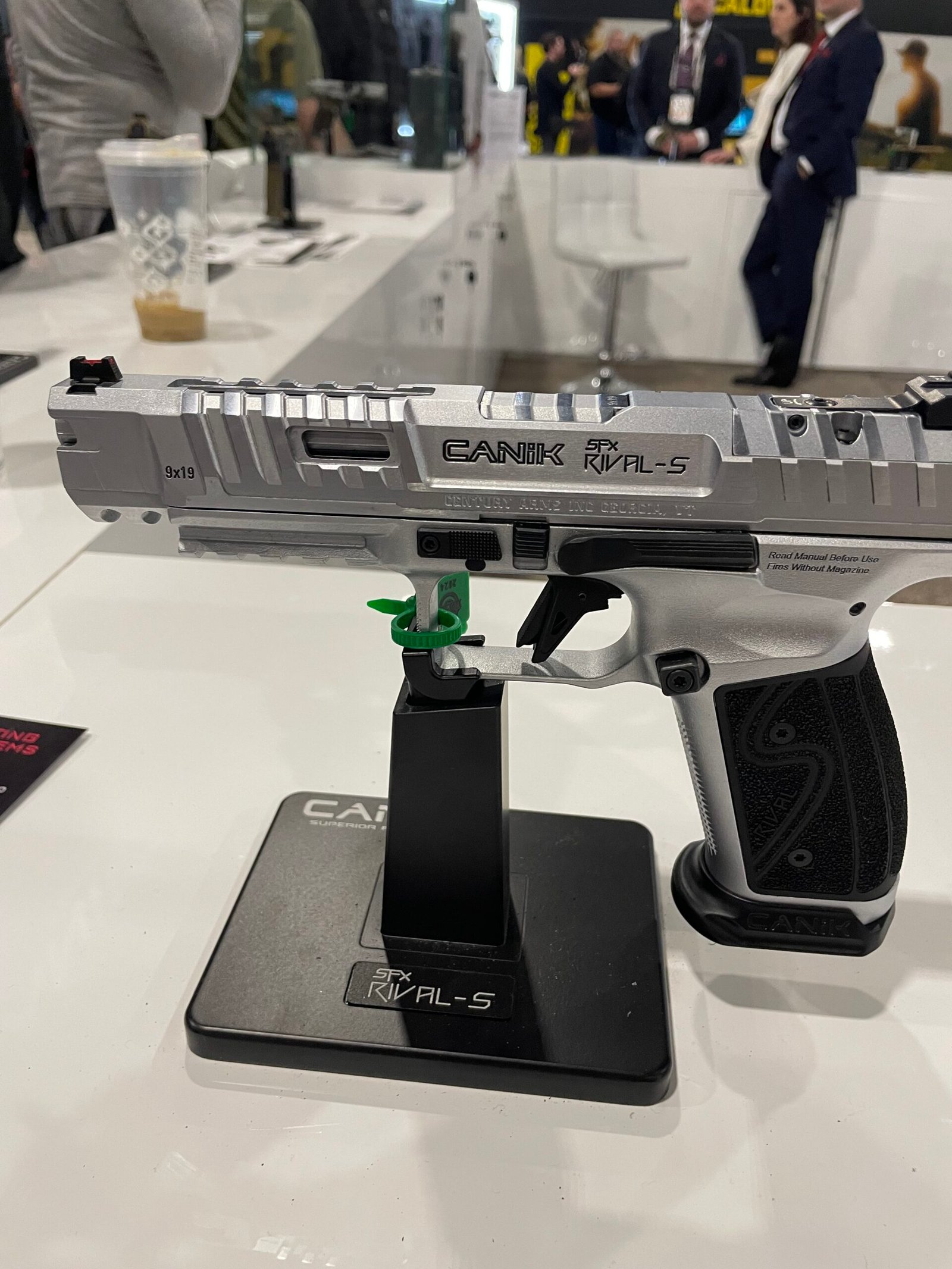 Detalhes de pistolas Canik expostas em suporte durante feira.