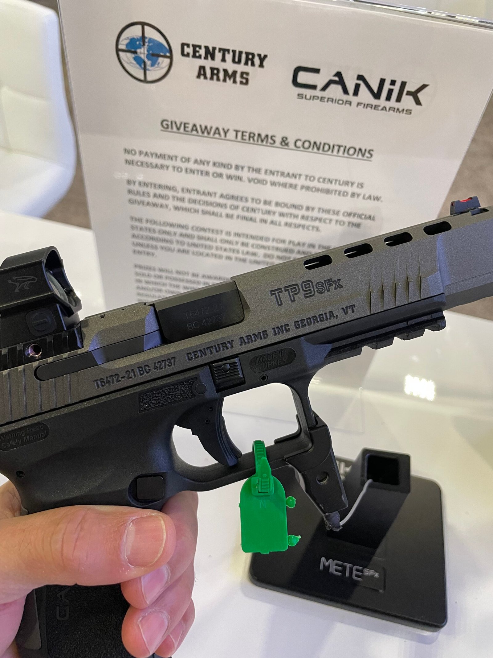 Detalhes de pistolas Canik expostas em suporte durante feira.