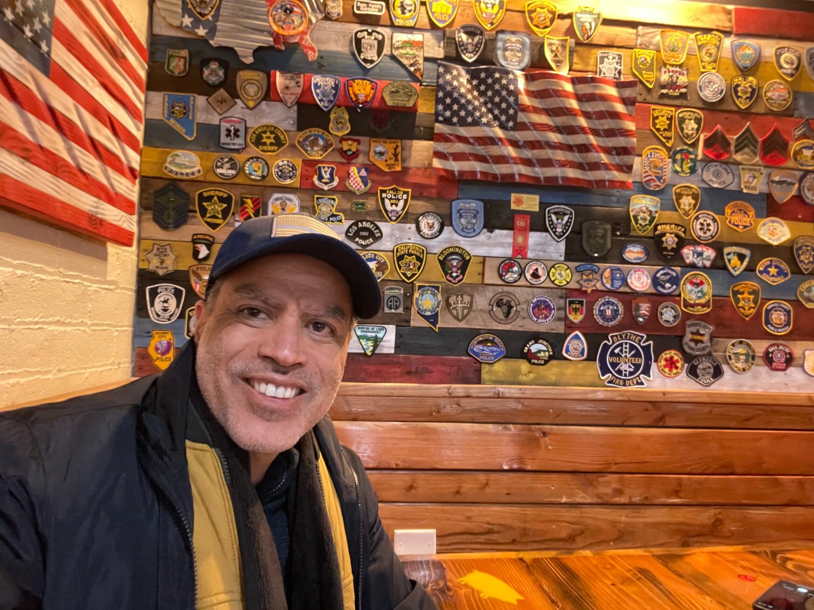 Demetrius Oliveira tira selfie diante de parede com distintivos policiais.