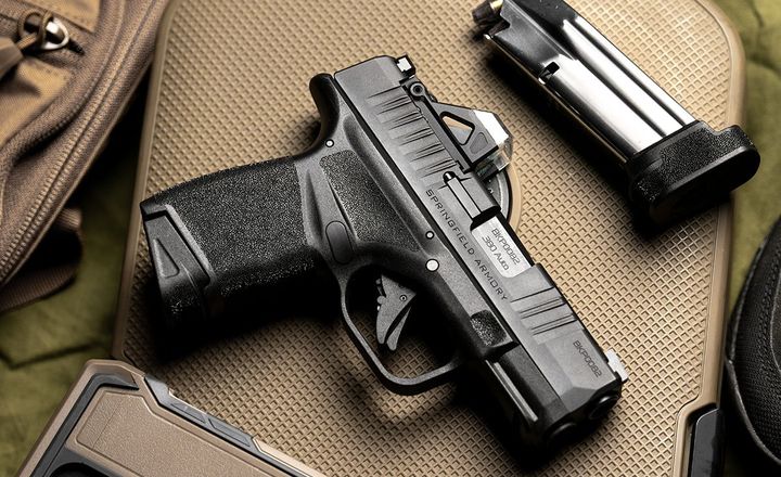 Pistola Springfield Armory Hellcat, carregador e celular sobre bolsa tática.
