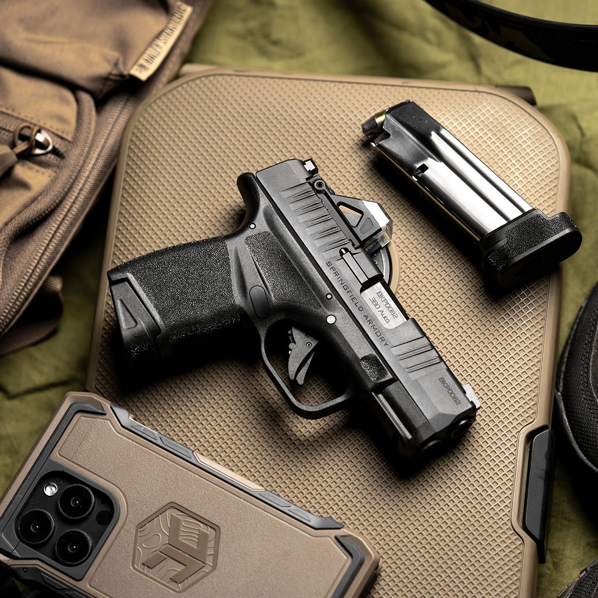 Pistola Springfield Armory Hellcat, carregador e celular sobre bolsa tática.