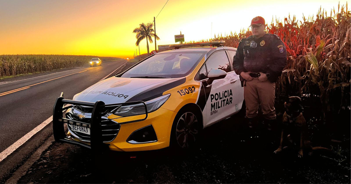 Policial militar ao lado de viatura em rodovia durante o pôr do sol.