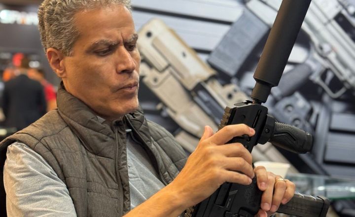 Demetrius Oliveira examina uma arma equipada com silenciador em feira.