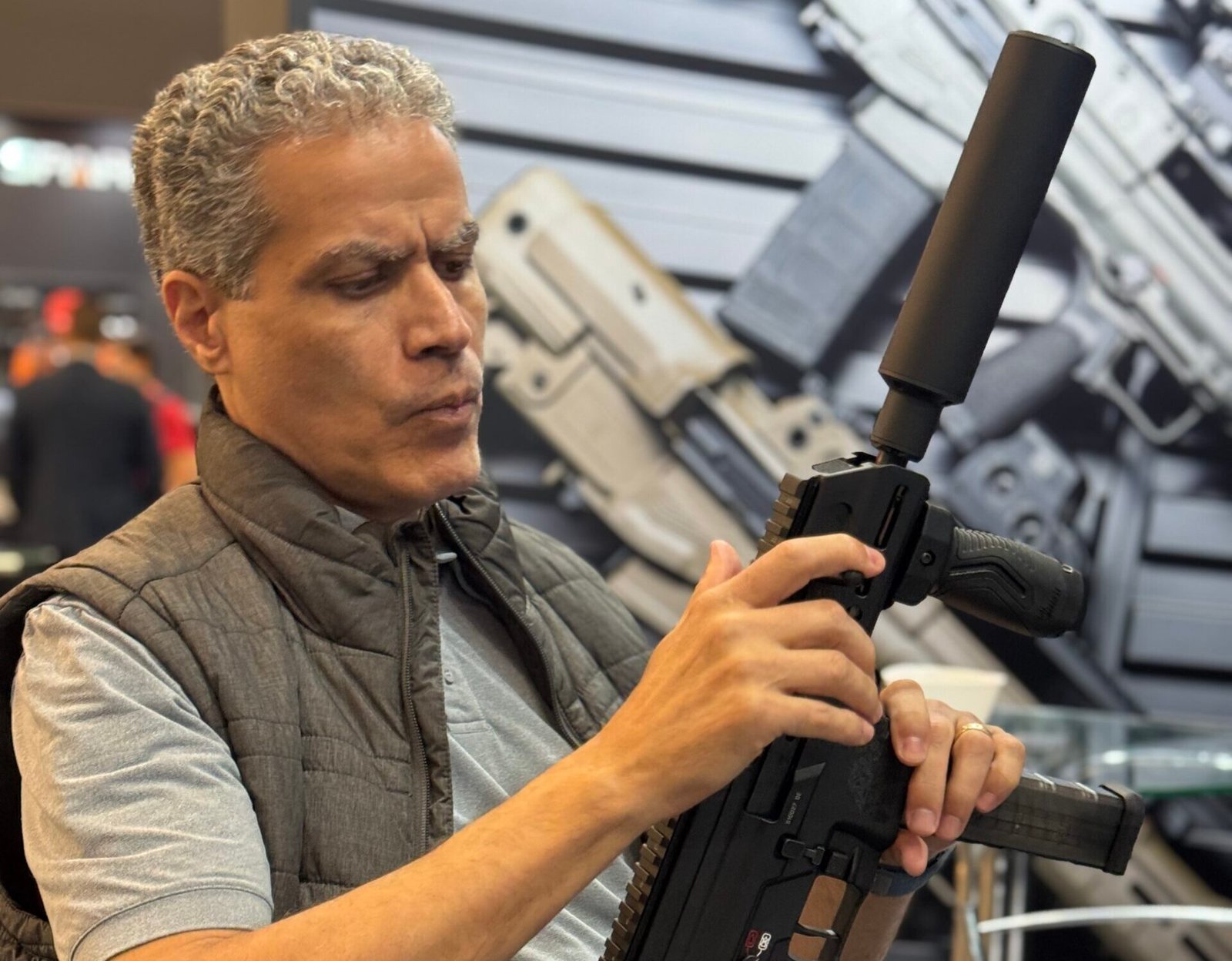 Demetrius Oliveira examina uma arma equipada com silenciador em feira.