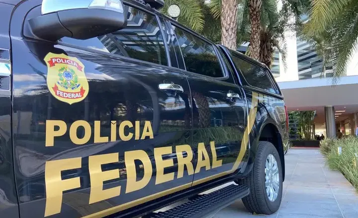 Viatura da Polícia Federal estacionada diante de edifício.