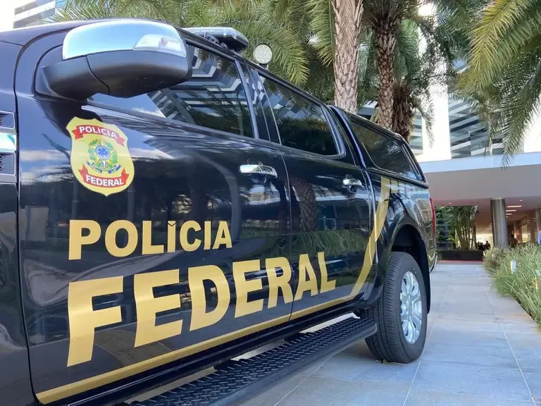 Viatura da Polícia Federal estacionada diante de edifício.