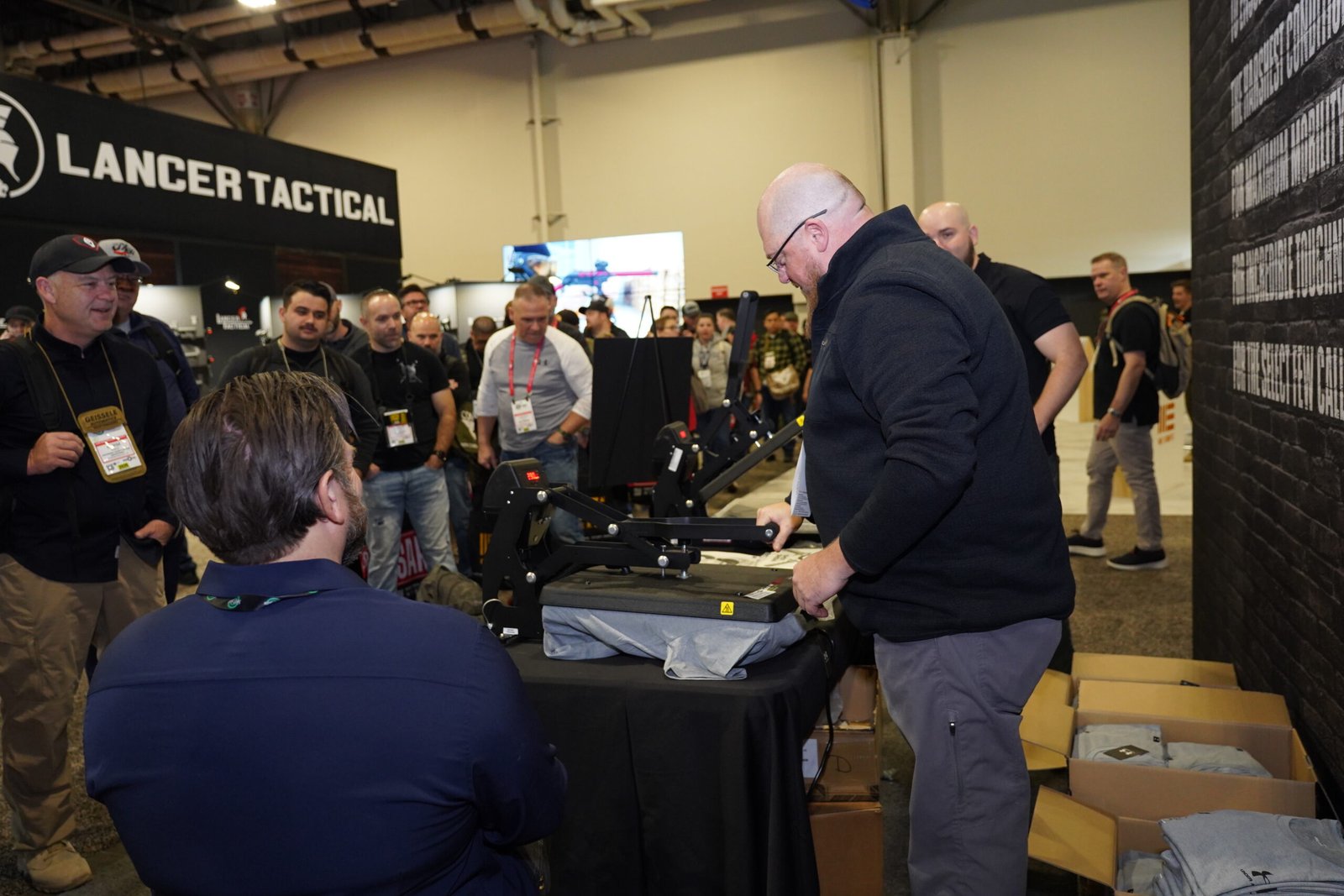 Expositor atende visitantes em mesa de equipamentos táticos.
