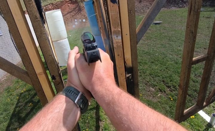 Atirador aponta uma pistola equipada com mira em uma pista de competição.