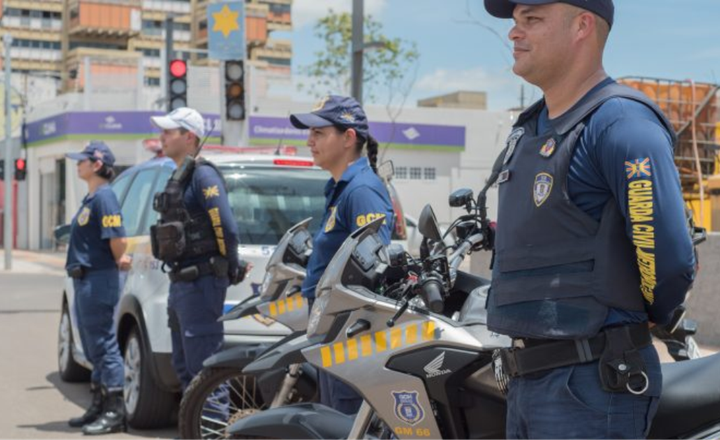 Guardas civis municipais trabalham junto a motocicletas em uma via urbana.