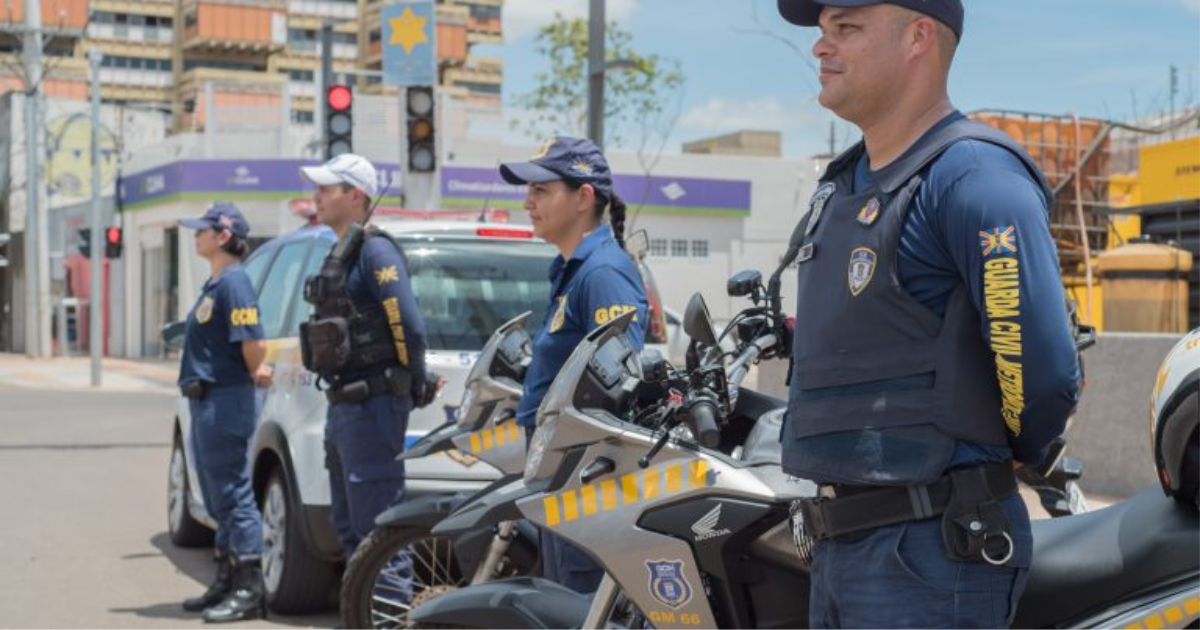 Guardas civis municipais trabalham junto a motocicletas em uma via urbana.