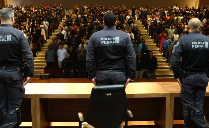 Policiais penais diante de auditório lotado durante cerimônia.