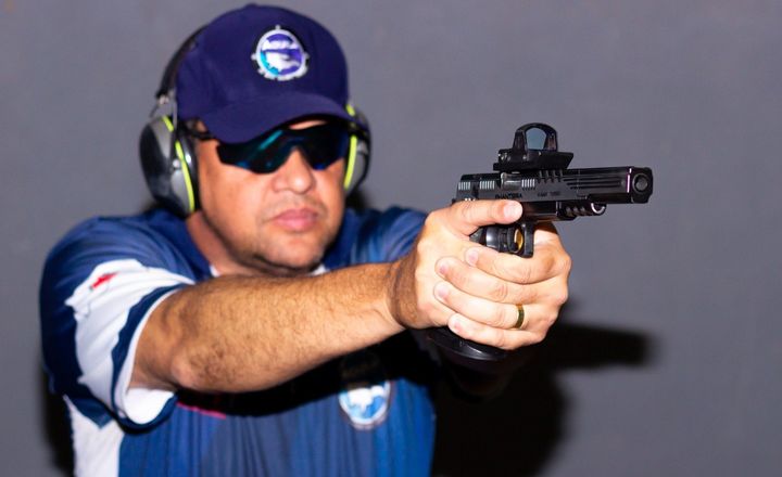 Leandro Boaventura pratica tiro com pistola equipada com mira.