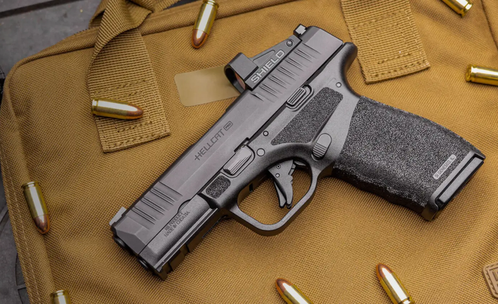 Pistola Hellcat Pro e cartuchos sobre uma bolsa tática marrom.
